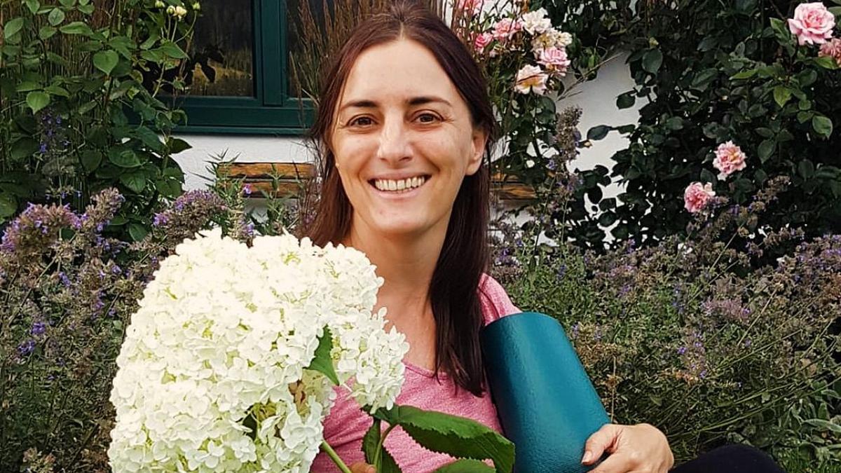 Nathalie Hosp mit Yogamatte und Blumen im Garten – Yoga Ausbildung in Innsbruck
